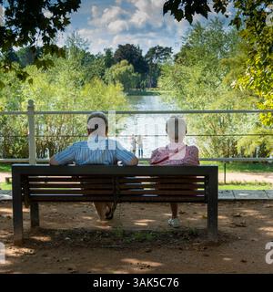 Vichy. Zwei ältere Menschen sitzen auf einer Bank und blicken auf den Fluss Allier, während ein junges Paar in der Nähe Erinnerungen festhält. Allier. Auvergne . Frankreich Stockfoto