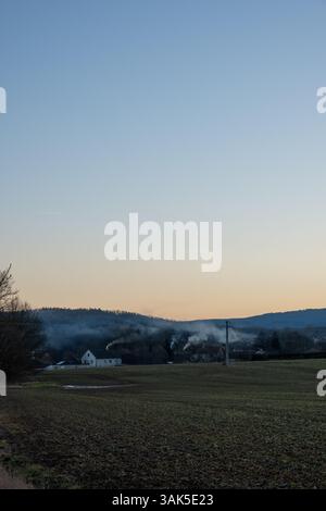 Rauch steigt bei Sonnenuntergang aus Schornsteinen auf Stockfoto