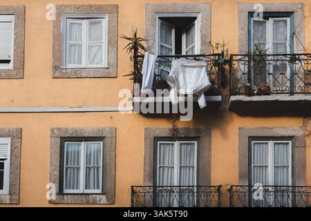 Die Wäscherei hängt zum Trocknen auf einem malerischen Balkon in Bairro Alto, Lissabon, mit Pflanzen geschmückt und von rustikalen Steinfenstern eingerahmt, die das Erbe der Stadt widerspiegeln Stockfoto
