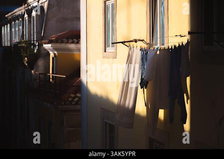 Die Wäsche hängt zum Trocknen an einer Wäscheleine vor einem gelben Gebäude in Bairro Alto, Lissabon, wo sie sich im goldenen Stundenlicht sonnt und die Ruhe einfängt Stockfoto
