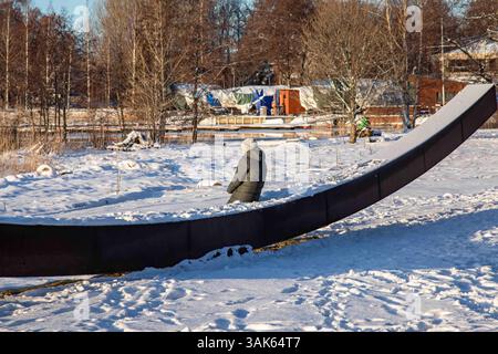 Frau sitzt auf dem schneebedeckten Helsinki Arch, einer Stahlskulptur von Bernard Kirschenbaum, im Bezirk Vähä-Meilahti in Helsinki, Finnland Stockfoto