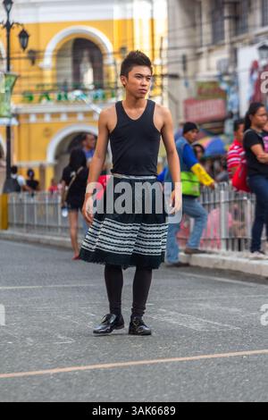 Ein männliches Model mit Rock geht selbstbewusst auf einer Straße in Iloilo City während einer Outdoor-Modeschau in einem öffentlichen städtischen Umfeld entlang Stockfoto