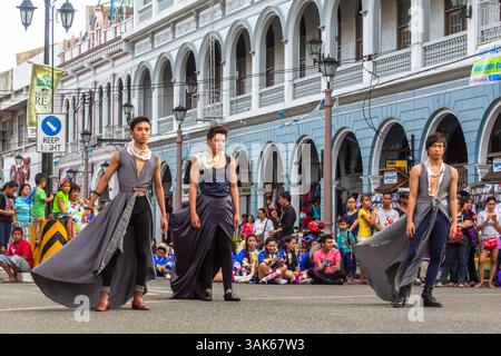 Männliche Models mit Rock gehen selbstbewusst auf einer Straße in Iloilo City während einer Outdoor-Modeschau in einem öffentlichen städtischen Umfeld entlang Stockfoto