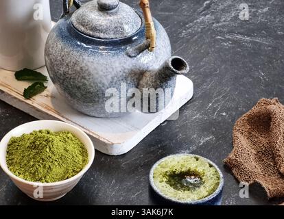 Erfrischender Matcha Latte in einem Keramikglas, neben einer Schüssel mit hellgrünem Matcha-Pulver und Keramik-Teekanne. Modernes und minimalistisches Ambiente. Für die Gesundheit Stockfoto