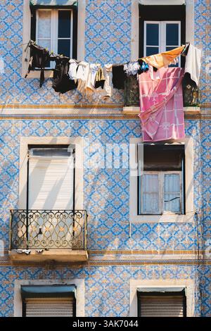 Die Wäsche hängt an einer Wäscheleine vor einem Wohngebäude in Lissabon, Portugal, mit dekorativen Keramikfliesen und einem traditionellen Balkon, Re Stockfoto