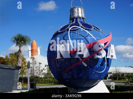 Eine blaue Metallkugel mit dem NASA-Logo steht am Eingang des Kennedy Space Center in Cape Canaveral, Florida, mit dem Space Shuttle im Hintergrund Stockfoto