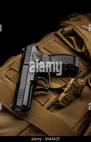 Schwarze taktische Pistole auf braunem Militärrucksack, Ansicht von oben nach unten, dramatischer Kontrast vor dunklem Hintergrund Stockfoto