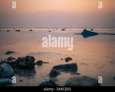 Malerischer Sonnenuntergang über ruhigen Gewässern mit Felsen und Reflektionen Stockfoto