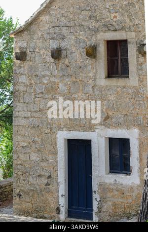 Ein bezauberndes rustikales Steinhaus mit blauer Tür und weißen Akzenten, eingebettet zwischen grünem Laub, strahlt ein gemütliches und traditionelles architektonisches Ambiente aus Stockfoto
