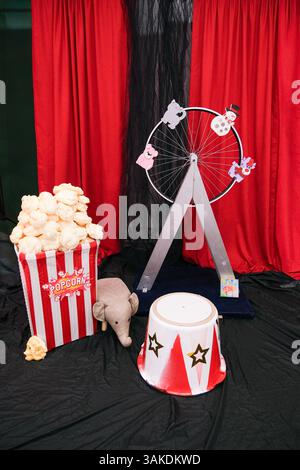 Eine Zirkusparty mit einem Popcorn-Eimer, einem kleinen Elefanten und einem rot-schwarzen Zirkusrad Stockfoto