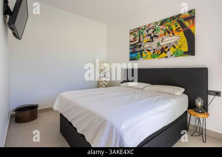 Modernes Zimmer mit auffälligen Street-Art-Gemälden über einem Doppelbett, Wandfernseher und minimalistischer Einrichtung. Stockfoto