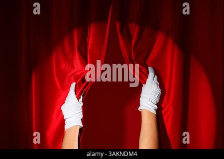 Weibliche Hände in weißen Handschuhen öffnen rote Vorhänge auf farbigem Hintergrund Stockfoto