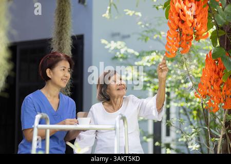 Lächelnde ältere Frau im Garten. Glückliche Seniorin, die sich auf der Terrasse mit einer Betreuerin zu Hause entspannt. Stockfoto