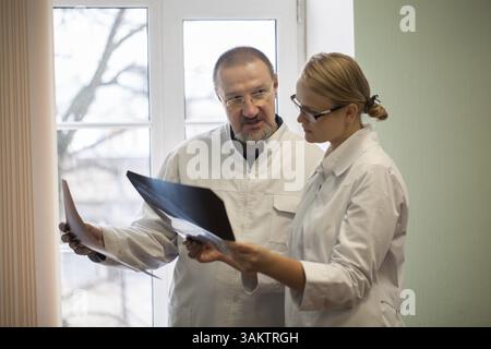Professor und junge Ärztin untersuchen und Vergleichen von zwei x-ray Bilder stehen durch das Fenster in der Klinik Stockfoto