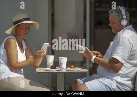 Während der Kaffeepause ist jeder mit Gadget beschäftigt. Reifer Mann und Frau mit Smartphone und digitalem Tablet im Café, wenn sie Kaffee mit Abendessen trinken Stockfoto