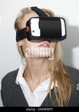 Junge blonde Frau in der erweiterten Realität, die mit Smart Phone Application virtuellen Raum erstellen Headset. Moderne unterhaltsame Technologien Stockfoto