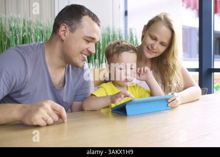 Familie mit Kind im Cafe. Mutter und Vater, Sohn, spielen auf der Kontaktschaltertafel Stockfoto