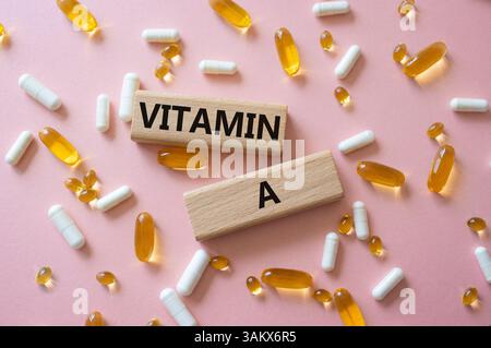 Vitamin-A-Symbol. Konzeptwort Vitamin A auf Holzblöcken. Schöner rosafarbener Hintergrund mit Pillen. Medizin und Vitamin-A-Konzept. Kopierbereich Stockfoto
