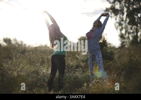 Zwei junge Frauen, die im Garten trainieren und Dehnungsübungen machen, um geschmeidig und fit zu bleiben Stockfoto