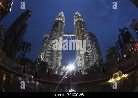 Weitwinkel- und Niedrigwinkelaufnahme von Personen vor den Petronas Twin Towers, beleuchtet bei Nacht. Kuala Lumpur, Malaysia, Asien Stockfoto