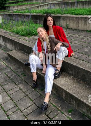 Weibliche Freunde sitzen auf Betontreppen und umarmen sich gegenseitig, Blick aus einem hohen Winkel an einem sonnigen Sommertag Stockfoto