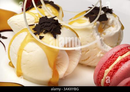 Gourmet Vanille Eis beträufelt mit Honig oder fruchtigen Sirup und gekrönt mit Schokolade Flocken mit bunten Rosa Makronen und eine Schokolade Whirl Stockfoto