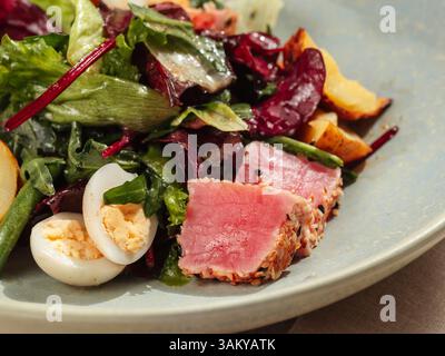 Thunfischsalat nach asiatischer Art mit Salat, Eiern, Kirschtomaten, Kartoffeln und Thunfischstücken in Sesamsamen. Gesunder Thunfischsalat. Nahaufnahme. Stockfoto