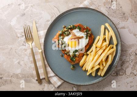 Leckeres heißes Schnitzel Holstein serviert mit Spiegelei, Sardellen- und ZitronenPetersiliensoße auf dem Teller auf dem Tisch. Horizontal oben Stockfoto
