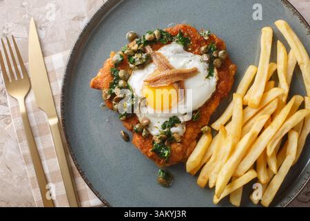 Schnitzel Holstein besteht aus einem panierten Schnitzel, das mit einem Spiegelei, Sardellen und zitroniger Kapernsauce auf dem Teller auf dem Tisch serviert wird. Hor Stockfoto