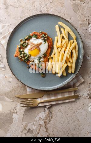 Deutsches Schnitzel holstein mit Spiegelei, Sardellen und zitroniger Kapernsauce ganz oben auf dem Teller auf dem Tisch servieren. Vertikale Draufsicht von oben Stockfoto