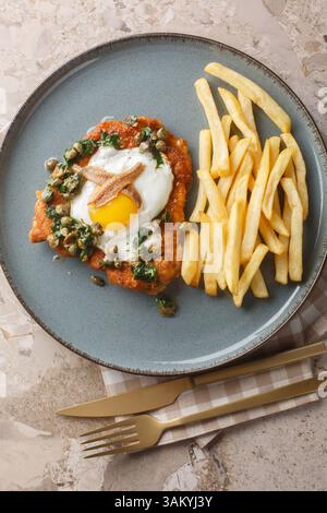 Schnitzel Holstein mit Spiegelei, Sardellen, Kapern und ZitronenPetersilie-brauner Butter serviert mit Pommes Frites auf dem Teller auf dem Tisch. Ver Stockfoto