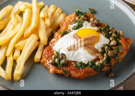 Schnitzel Holstein besteht aus einem panierten Schnitzel, das mit einem Spiegelei, Sardellen und zitroniger Kapernsauce auf dem Teller auf dem Tisch serviert wird. Hor Stockfoto