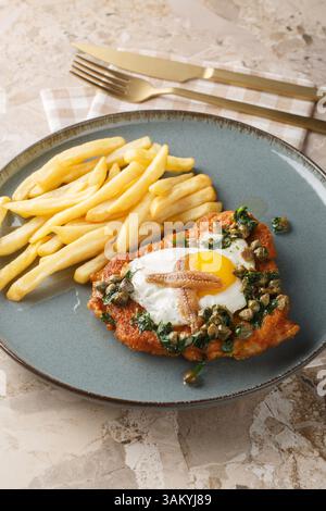 Deutsches Schnitzel holstein mit Spiegelei, Sardellen und zitroniger Kapernsauce ganz oben auf dem Teller auf dem Tisch servieren. Vertikal Stockfoto