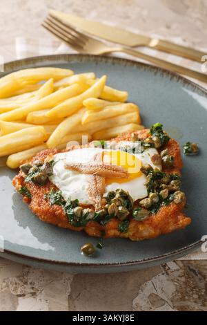 Schnitzel Holstein mit Spiegelei, Sardellen, Kapern und ZitronenPetersilie-brauner Butter serviert mit Pommes Frites auf dem Teller auf dem Tisch. Ver Stockfoto