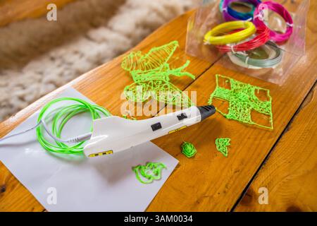 3D-Druckstift und bunte Filamente auf Holztisch mit grüner Schmetterlingsform, selektiver Fokus Stockfoto