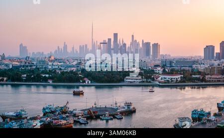 Der Hafen von Dubai Creek bietet einen atemberaubenden Blick auf die Skyline von Dubai bei einem wunderschönen Sonnenuntergang, mit traditionellen Booten, die auf dem Wasser segeln und modernen Archi Stockfoto