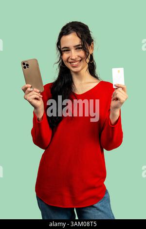 Glückliche junge Frau hält ein Smartphone und eine Kreditkarte in der Hand, was Online-Shopping und sichere Bezahlung vorschlägt Stockfoto