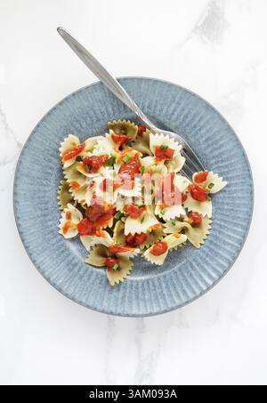 Ein Teller mit gekochter Farfalle-Pasta mit Tomatensauce auf weißem Marmortisch Stockfoto