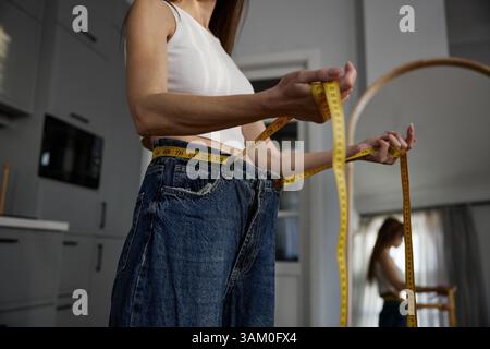 Mittelteil-Aufnahme einer dünnen Frau, die Jeans mit Maßband trägt Stockfoto