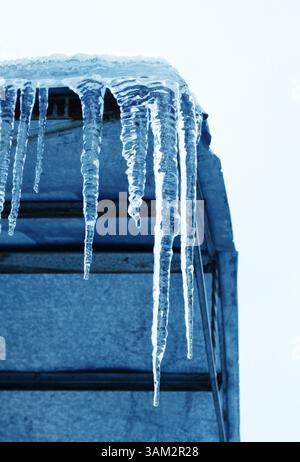 Nahaufnahme großer Eiszapfen, die vom Dach an der Ecke des Gebäudes hängen Stockfoto