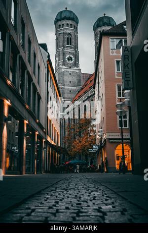 Beleuchtete Kopfsteinpflasterstraße, die zur entfernten Münchner Kirche führt Stockfoto