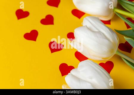Drei weiße Tulpen auf gelbem Papier mit roten Herzen, roten Herzen und weißen Tulpenblüten auf gelbem Papier, Nahaufnahme Stockfoto