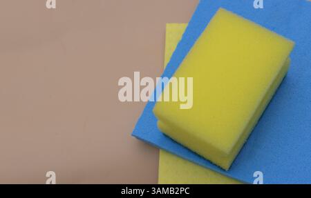 Auf dem Tisch befindet sich ein blau-gelber Schwamm, der zwei verschiedene Farben hat. Die Hintergrundfarbe sollte hellbraun oder beige sein. Stockfoto