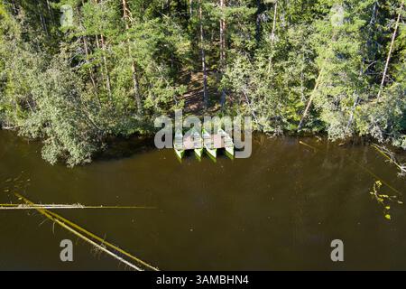 Luftaufnahme: Vier grüne Kanus, die an einem hölzernen Dock an einem Waldfluss oder Seeufer vertäut sind. Stockfoto