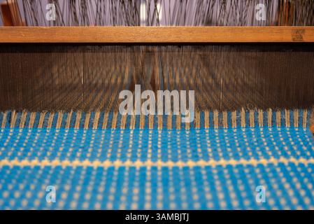 Blauer Vintage-Faden hinter einem manuellen Holzwebstuhl, alter Webstuhl. Hochwertige Fotos Stockfoto