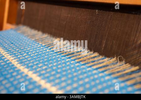 Blauer Vintage-Faden hinter einem manuellen Holzwebstuhl, alter Webstuhl. Hochwertige Fotos Stockfoto