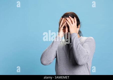 Ein entsetzter junger Kerl, der schockiert ist und sich um etwas sorgt, verzweifelt und ängstlich vor blauem Hintergrund ist. Ängstlicher, verängstigter Mann, schreckliche Reaktion. Stockfoto