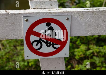 Ein Schild ohne Radfahren, das auf einem weißen Holzzaun vor einem grünen grünen grünen Hintergrund in einem Naturpark montiert ist Stockfoto
