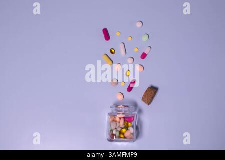 Draufsicht im Winkel eines Gefäßes mit Pillen, von denen einige auf eine weiße Oberfläche verschüttet wurden Stockfoto