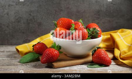 Erdbeerkonzept mit einer Gruppe reifer roter Erdbeeren in einer weißen Schale Nahaufnahme Frontansicht auf einem rustikalen Holztisch im Vintage-Stil und grauem Hintergrund. Stockfoto